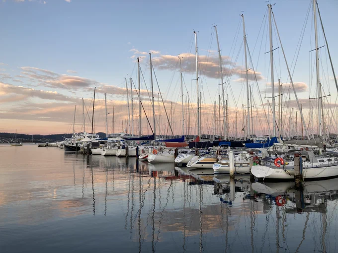 Sunset over the Eastern Shore of the Derwent river, showing pinky clouds in the sky and reflected in the water, and boats in the foreground