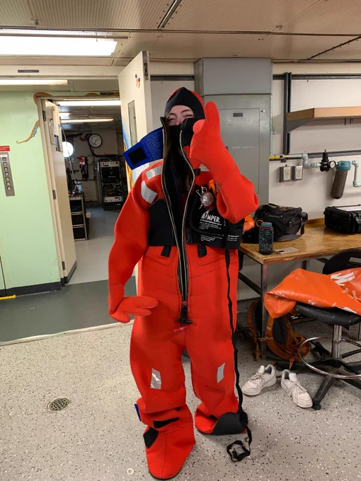 PNSN staff member aboard research vessel in half-zipped bright orange immersion suit.