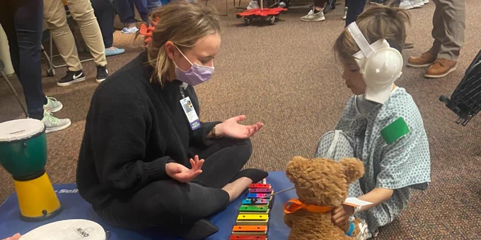 A young child plays the xylophone on the floor with a Child Life specialist. 