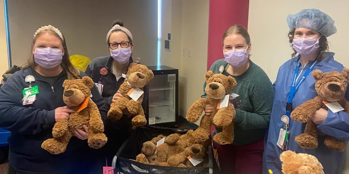 4 Child Life specialists hold teddy bears at a table during the Teddy Bear Clinic. 