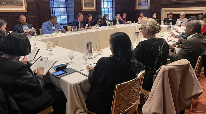 A group of diverse men and women sit at tables arranged in a rectangle.