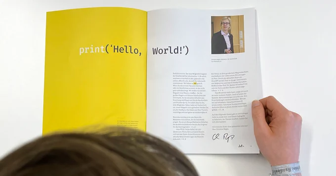 Eine Person, die im aufgeschlagenen GI-Mitgliedermagazin .inf blättert. Zu sehen ist der Schriftzug "Hello, world".