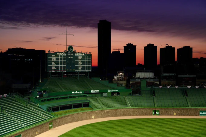 The sun rises in Chicago, portraying a beautiful silhouette of the Lakeview neighborhood behind the Wrigley Field scoreboard - it's the dawn of a new season. 
