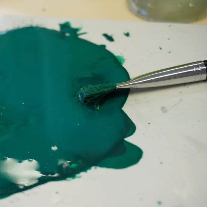 Close up shot of the tile and paint preparation. On the left there is a puddle of bright green paint, on the right there is a brush with green colour on the tip.