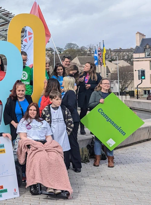 Single parent Angela with her lovely supportive son Kyle wearing OPFS t-shirts. Someone holding @CAPScot 'Compassion' sign. @PovertyAlliance flag in background.