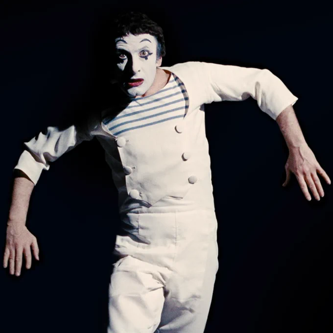 Mime Marcel Marceau wearing a white jumpsuit and a striped shirt 