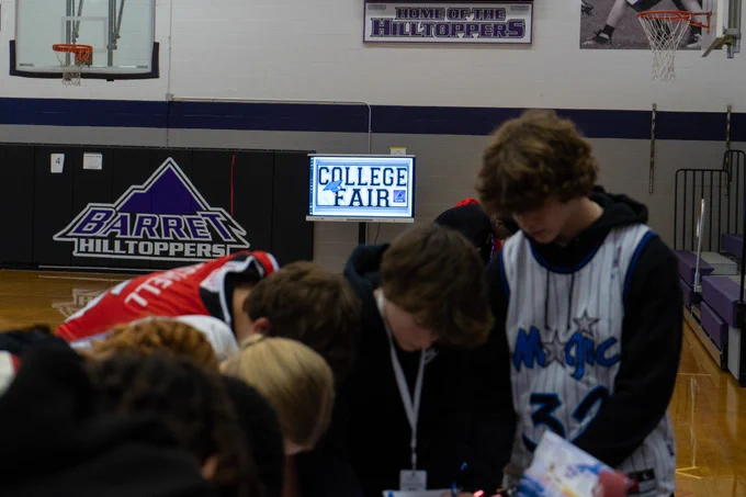 Students stand at a table with a College Fair sign in the background.