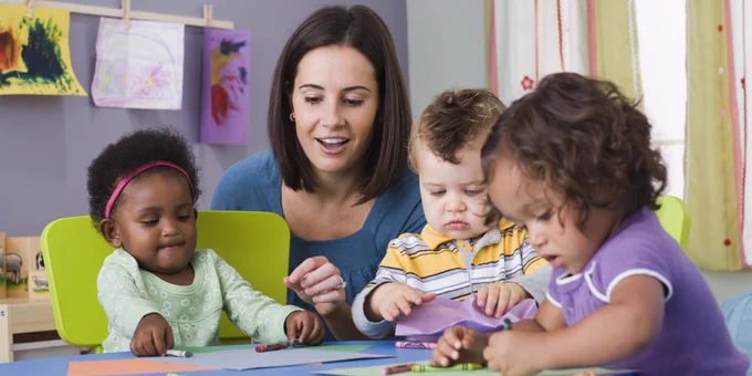 Three toddlers sitting at a table with their teacher