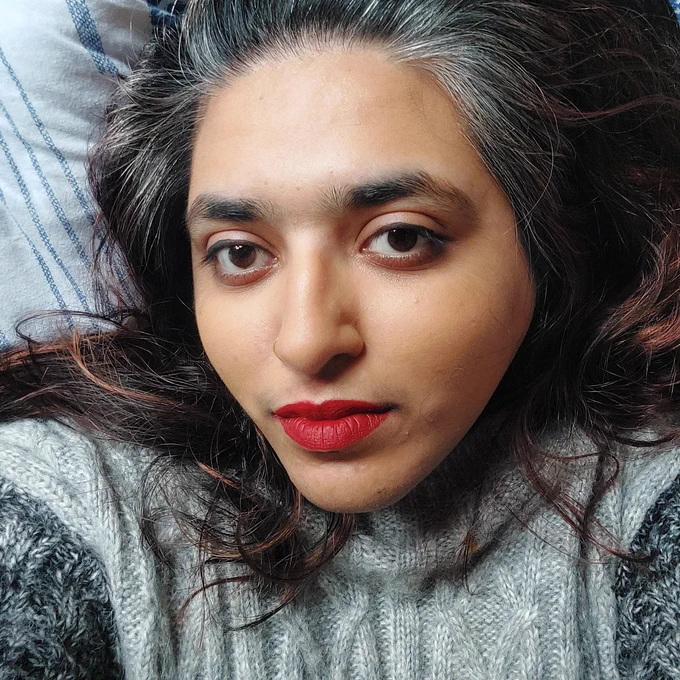 Selfie of a woman wearing a grey cable-knit jumper and red lipstick. Her long brown hair spills over her shoulders. She looks directly at the camera. 