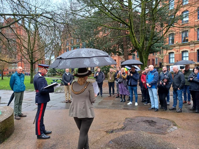 A photo of the Lord Mayor, stood under an umbrella, facing a crowd of people in Sackville Gardens  