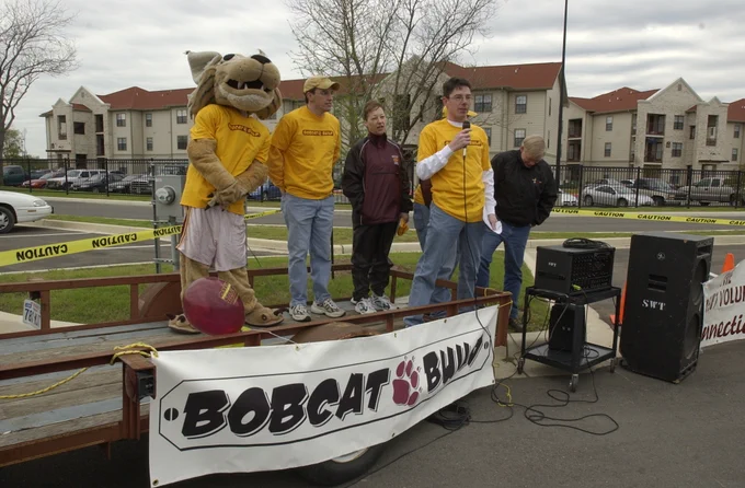 Bobcat mascot and three people on a makeshift stage with a microphone