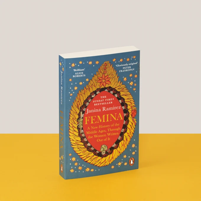 A paperback version of Femina sits on a yellow surface with a grey background. The cover reads 'FEMINA: A New History of the Middle Ages, Through the Women Written Out of it.'