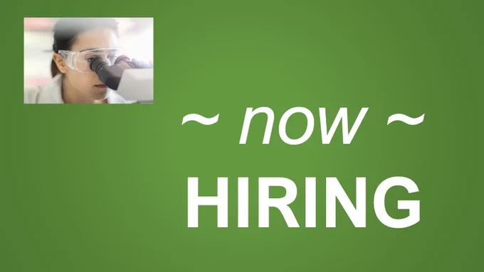 In the upper left part of the picture, a woman wearing a lab coat and safety glasses looks into a microscope.  In the lower right part of the picture, large white text says, "now HIRING".  Picture background is dark green.