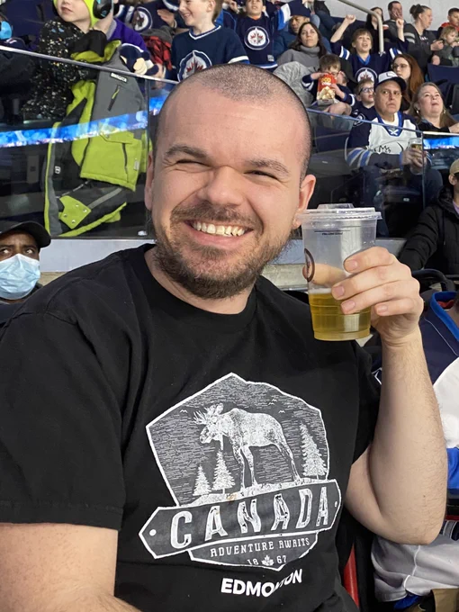 Smiling man at hockey game holding a drink up.