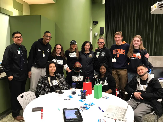 Deaf and hard of hearing students participate in the hackathon and are seated around a round table. Jose, their instructor, Jill Stark, Shireen Hafeez, Rachel Arfa and Sarah Faber of Parks join the students in smiling for the camera.