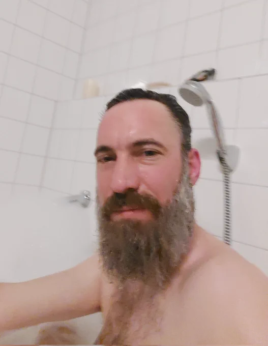 LeChral sitzt in der Badewanne und schmunzelt ganz leicht. Der Bart ist dunkel und grau-meliert. Es scheint heiß zu sein, denn das Bild ist vom Wasserdampf leicht verschwommen. 