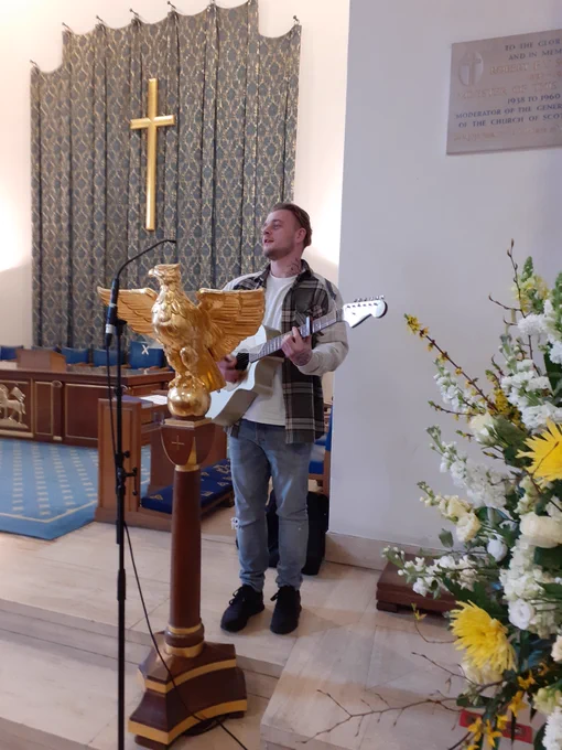 The photo shows musician Luke McCarthy performing at St Columba's church next to some lovely flowers 