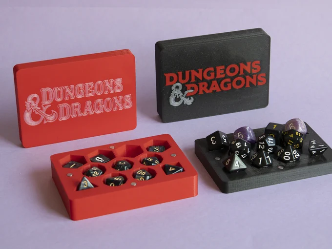 Two open 11-dice boxes. Left one is red, with the classic Basic D&D logo from Mentzer's edition, in silvery white. The cover that serves as tray is standing upright, while the bottom part of the box, with deep holes, is in its natural position. The right box is black, with the 5th edition full logo in red and silver: letters are red, the dragon ampersand is silver. In this one, it's the bottom part that's standing upright, while the cover-tray is in its usual working position, showing how the dice stand up in an easy-to-pick distribution.