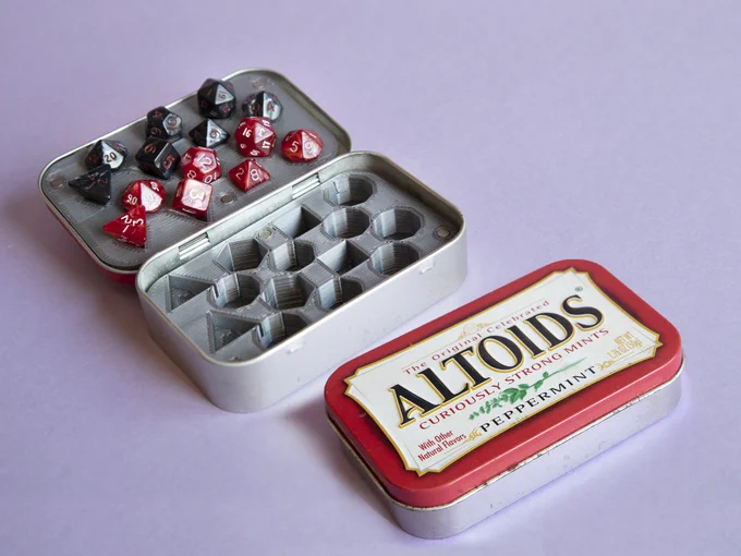 Two boxes of Altoids mints: top one is open, bottom one is closed. The open one displays a 2-part insert for dice, holding 2 sets of mini dice. One set is pearl red with white numbers, the other is pearly black with red numbers.
