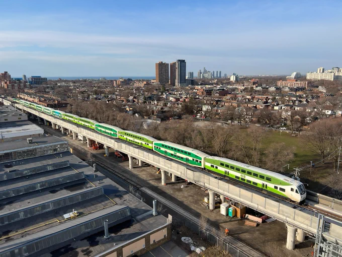 A GO Train travels across a new elevated guideway with the city in the background.