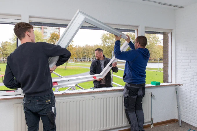 Drie mannen tillen een nieuw raam in het kozijn