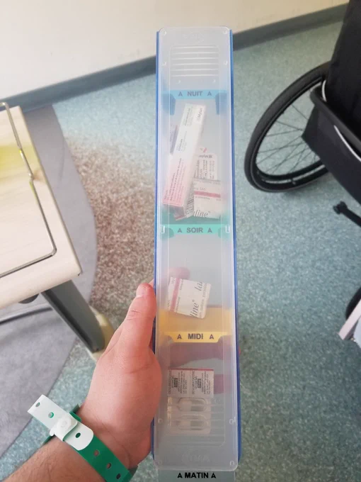 Je tiens dans ma main un très gros pilulier contenant les médicaments pour une journée. Il est trop large pour que je puisse refermer ma main entière et fait la taille de mon avant bras en longueur. 