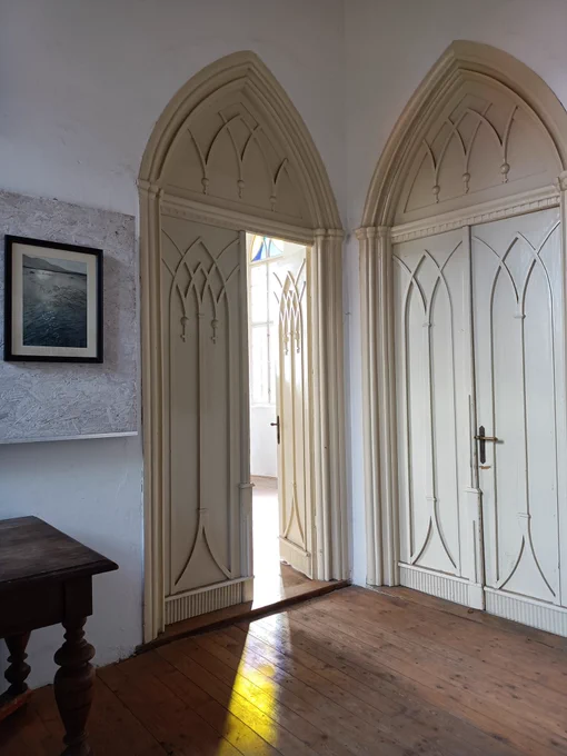 White high, gothic shape doors, stained glass window reflection on the hardwood floor