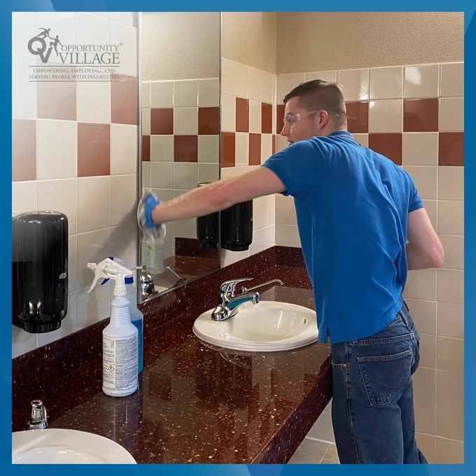 A man cleaning a mirror over a sink.