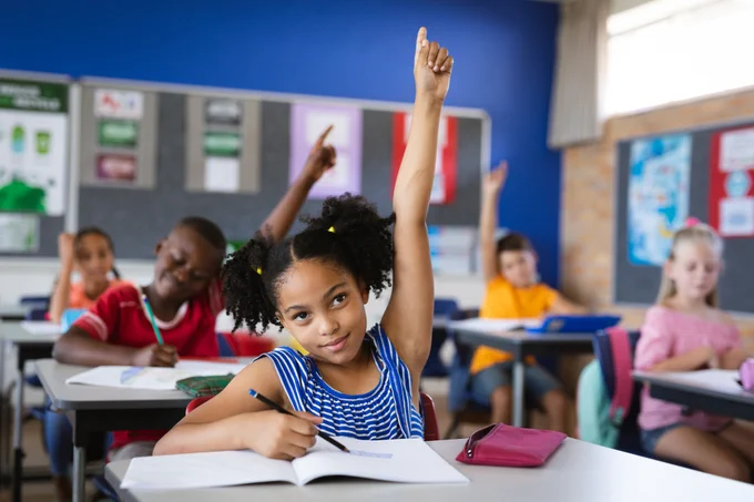 Girl raising her hands while sitting on her desk in the class at school