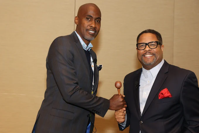 Tyrone Howard and Rich Milner stand holding a gavel between them and smiling at the camera.