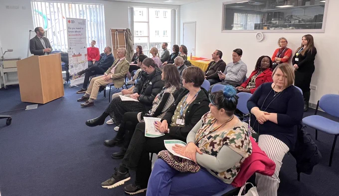 AccessAble's David Livermore addressing an audience at UHBW's AccessAble launch event. He is stood in front of a rostrum with a pull up banner stand to the right.