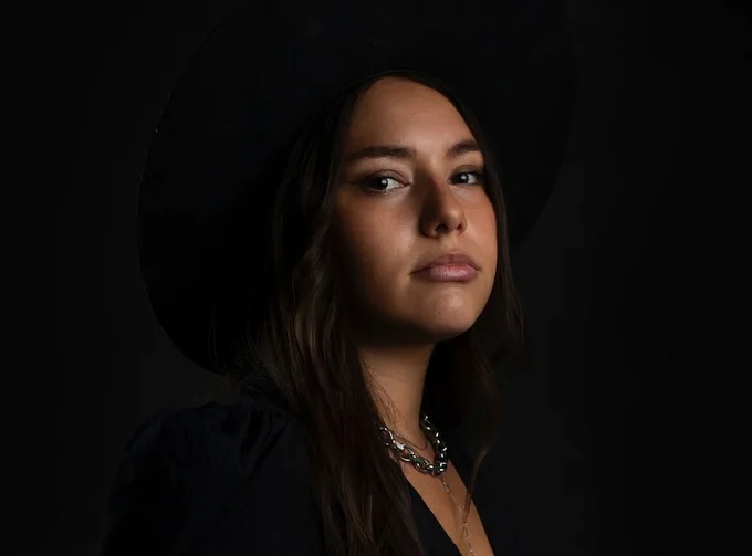 Image is of Suzanne Kite, she is wearing a black hat with a black top and has medium length brown hair.