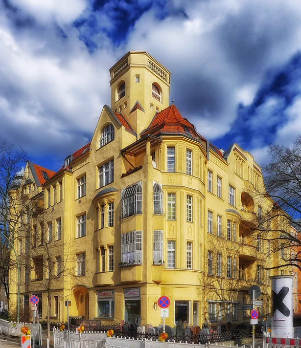 A bright yellow building in national romanticism architectural style standing on a street corner against the backdrop of a bright blue sky with white clouds