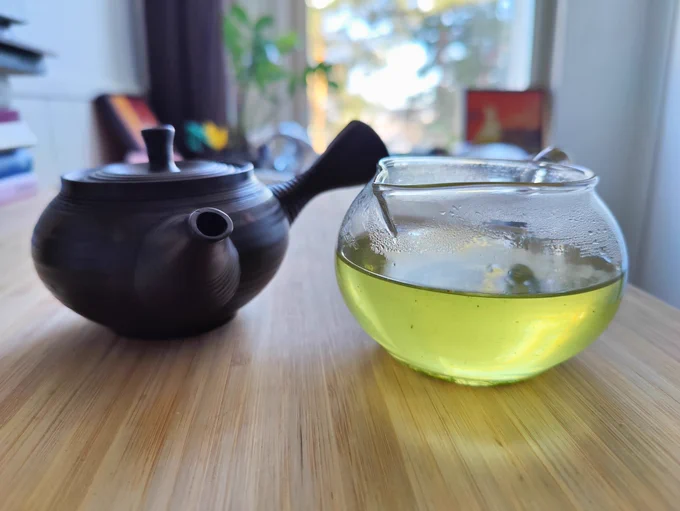 A small japanese teapot with a glass mug half-full of green tea next to it