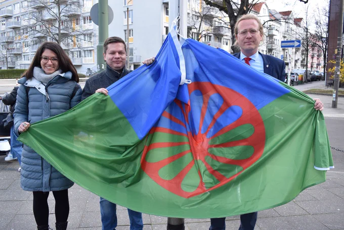 Die Bezirksamtsmitglieder Filiz Keküllüoğlu, Martin Schaefer und Kevin Hönicke mit der Roma-Flagge, die am Rathaus Lichtenberg anlässlich des Internationalen Tags der Roma gehisst wurde.