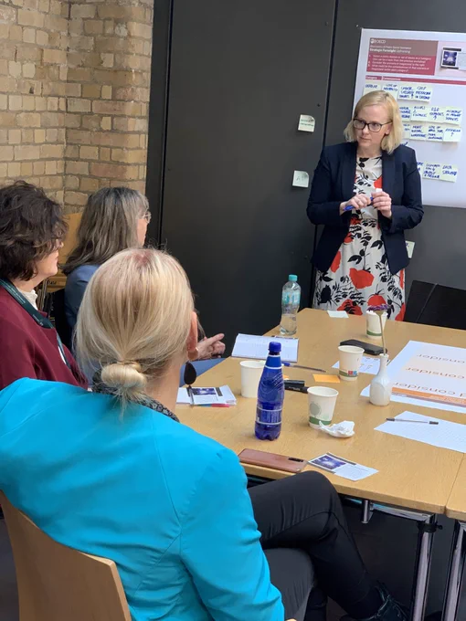 Piret Tõnurist facilitating a workshop, standing in front of a flip chart, while three participants watch