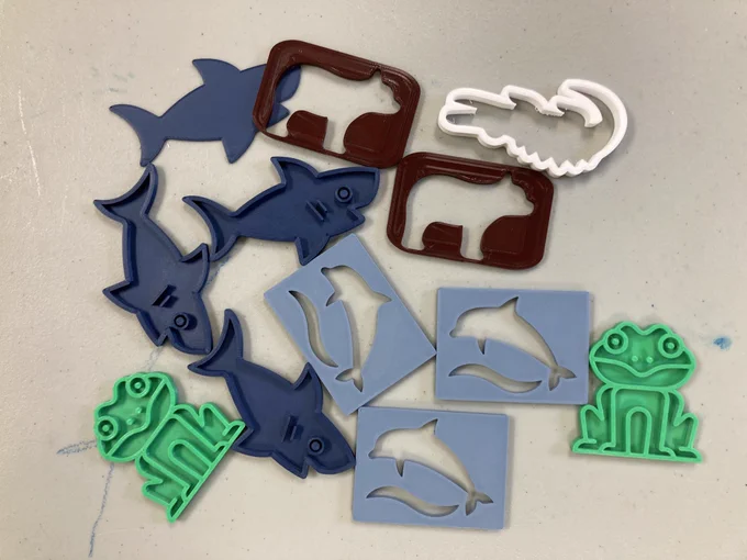 An assortment of play doh stencils. Shark, frog, bear, dolphin with a wave, and crocodile.