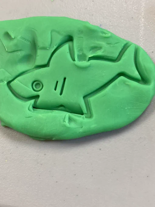 Happy looking shark stencil set on green play doh.
