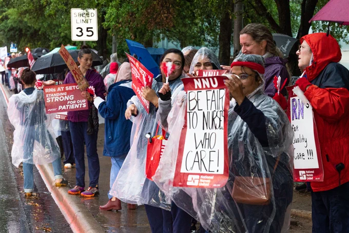 A large crowd of nurses stand in ponchos and with umbrellas in the rain at an info picket outside of Ascension Seton Medical Center in Austin, Texas. 