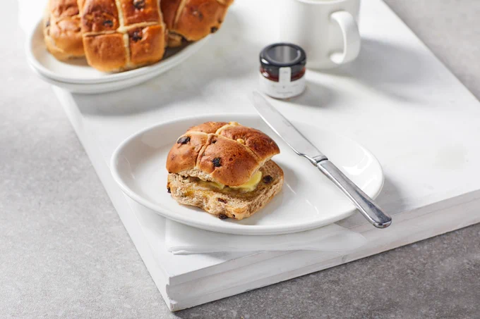 Our first class easter hot cross bun on a plate with jam and a mug