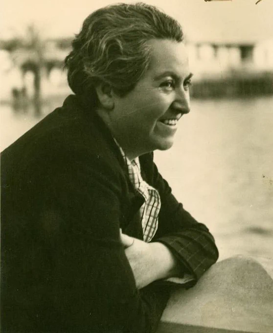 A sepia toned image of Gabriela Mistral leaning on a wall and smiling.