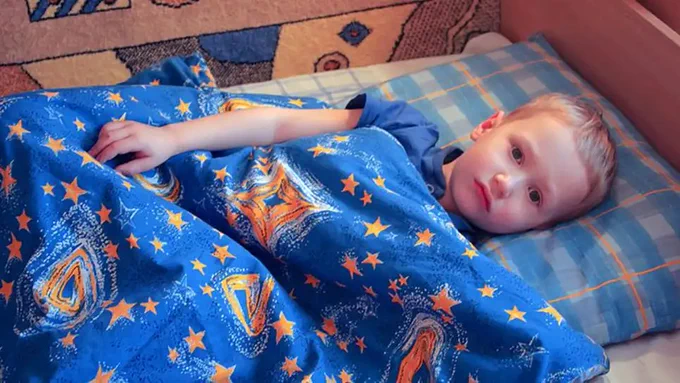 Young boy laying in his bed with space bedding.