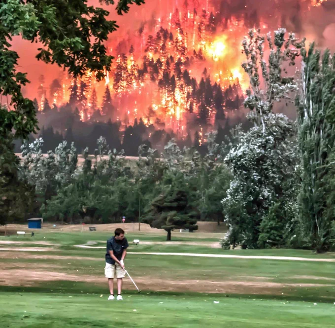 Ein Mann spielt Golf, während hinter ihm der Wald brennt.