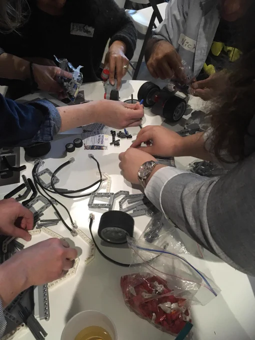 Image is of people sitting at a table putting together different parts to make a robot.