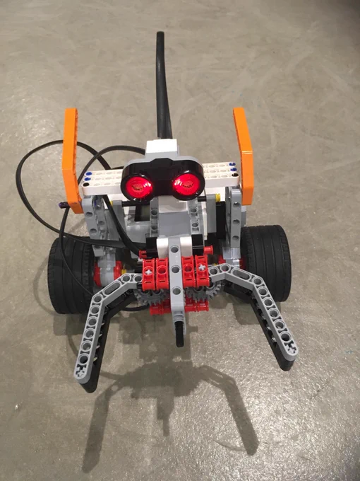 Image is of a small robot with wheels, red eyes, and  two clamps for "hands."