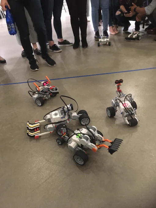 Image is of four small robots in a battle on the floor. All the robots have wheels and are charging one another. 