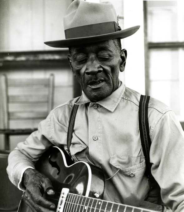 Black & white photograph of Mance Lipscomb playing the guitar.