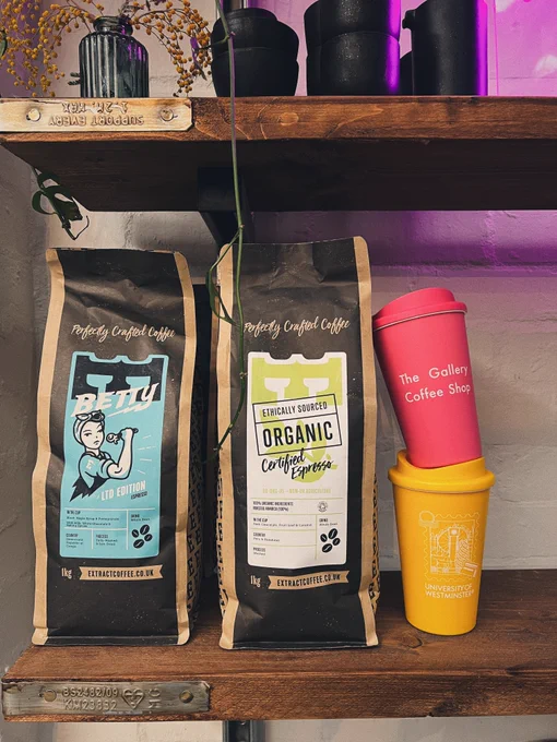 A pink and a yellow reusable cup are stacked against bags of Extract Coffee beans