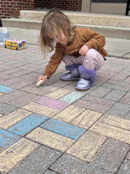 toddler colors the sidewalk with chalk