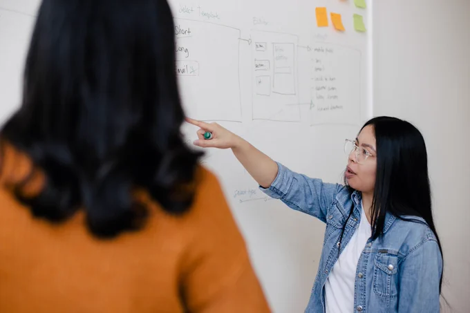 A woman points to a white board.